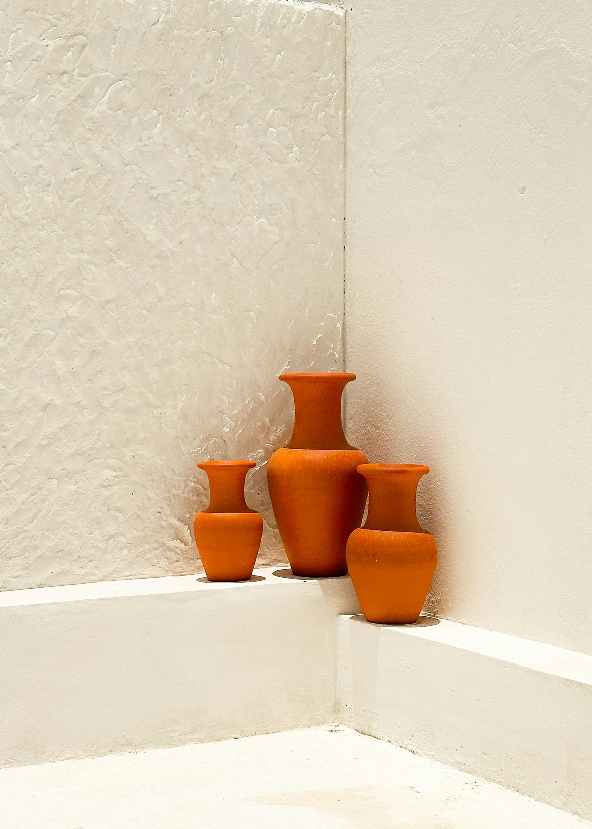 Orange terracotta-style vessels placed against plaster-textured wall