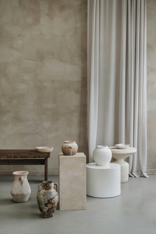 Stone or ceramic vases and pots placed on stone platform -white long curtain draping in background 