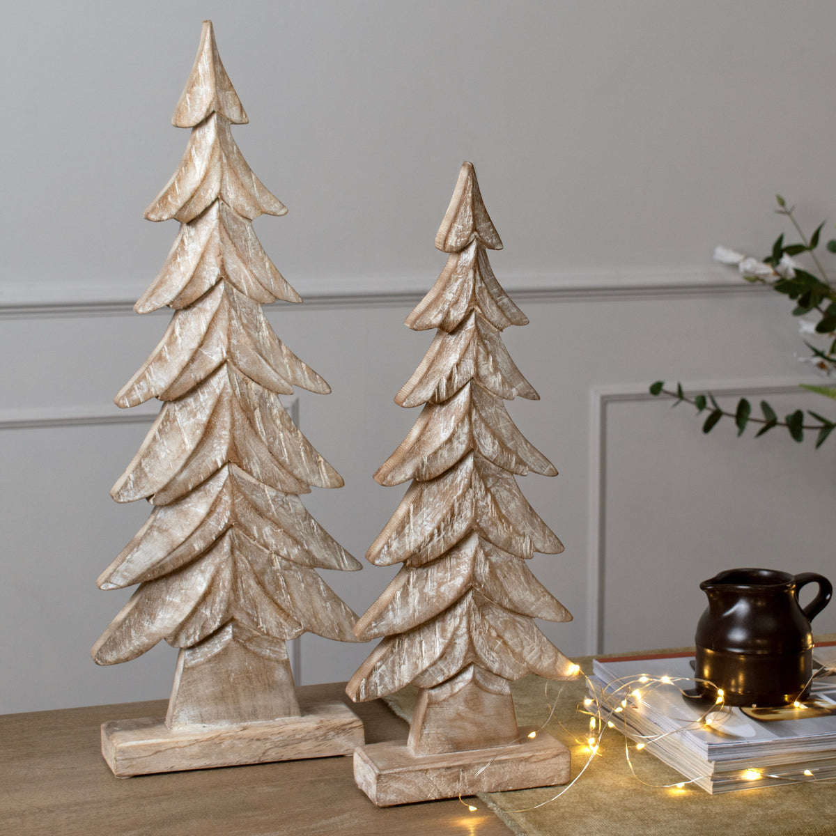 Two wooden Christmas tree decorations on a surface with a neutral background