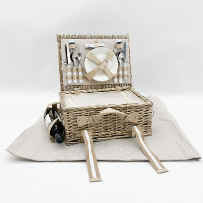 picnic basket  with plates and cutlery on a white  blanket - bottle of  wine on side  